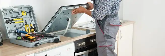 Cooktop repair technician lifting a built-in stovetop for service in Birmingham, AL