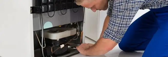 Refrigerator repair technician servicing the compressor and condenser area in Birmingham, AL