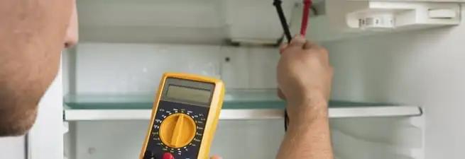 Refrigerator repair technician testing electrical components with a multimeter in Birmingham, AL